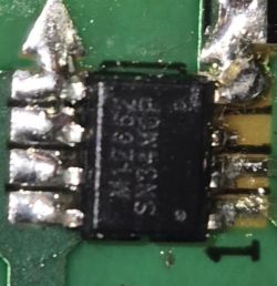 Zbliżenie na układ scalony SMD z nieczytelnym nadrukiem na zielonej płytce PCB