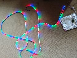 WS2811 LED strip glowing in rainbow colors, lying on a carpet with packaging and electronics.
