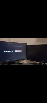 Dwa monitory na biurku, lewy wyświetla ekran startowy GIGABYTE z artefaktami graficznymi, prawy jest czarny.