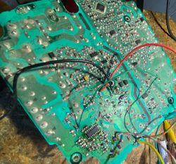 Damaged electronic circuit board with visible wires and solder traces.