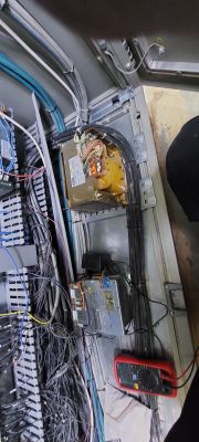 Wnętrze szafy sterowniczej z kablami, modułami i multimetrem.