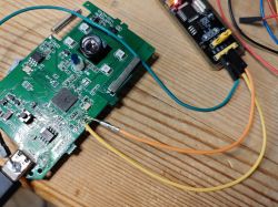 A printed circuit board with connected wires and a USB programmer on a wooden table.