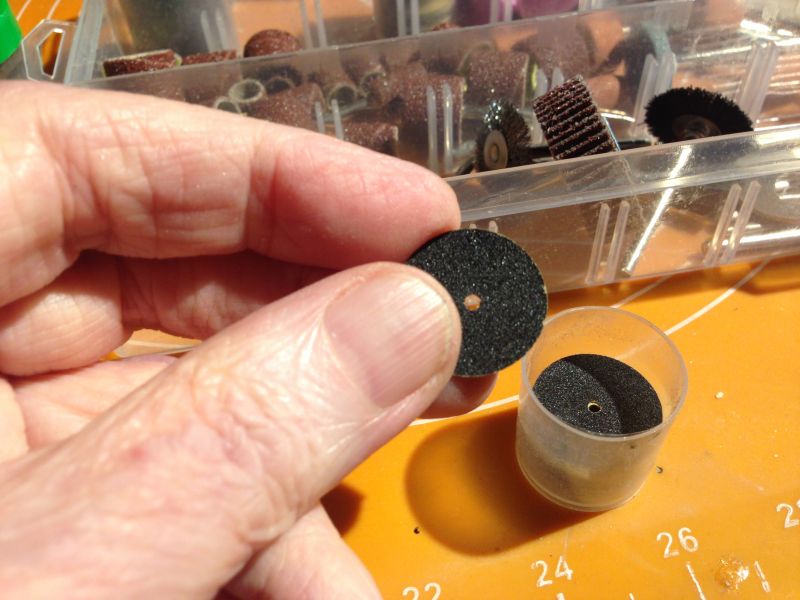 Ręka trzymająca cienką tarczę szlifierską, obok pudełko z dodatkowymi akcesoriami.
