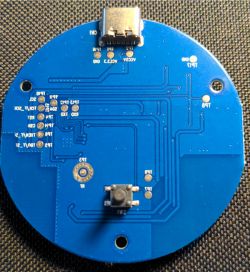 Blue round circuit board with USB-C port on top and a button at the bottom.