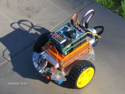 Small robot built on a wheeled platform with ESP32 and UNO boards, with LED display and visible wires.