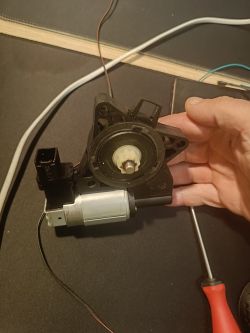 Ręka trzyma silniczek z kostką sześciopinową, obok leży śrubokręt.