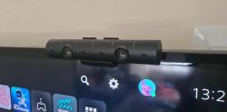Kamera PlayStation Camera zamontowana na górze telewizora z widocznym interfejsem PlayStation na ekranie.