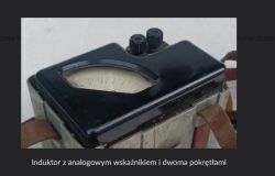 Zbliżenie na analogowy wskaźnik w obudowie i dwa czarne zaciski u góry urządzenia
