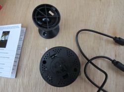 Small Spy Camera and Accessories on Table Small black camera or spy camera with cable, stand, and manual on a wooden table.