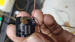 Hand holding a small electronic module with exposed PCB and red and black wires attached