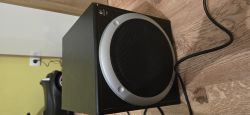 Czarny subwoofer Logitech Z560 z okrągłą metalową ramką i maskownicą, na drewnianej podłodze