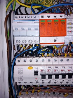 Zbliżenie na elektryczną rozdzielnię z różnymi elementami instalacji elektrycznej i kablami.
