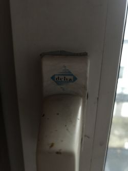 Biała klamka okna z logo firmy Delta.