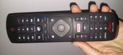 Pilot zdalnego sterowania Alizen RML1285 trzymany w dłoni, z licznymi przyciskami, w tym przyciskiem Netflix.