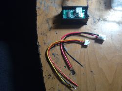 Otwarty moduł miernika z płytką PCB oraz wiązka przewodów z dwiema białymi wtyczkami na stole