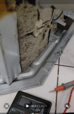 Wnętrze piekarnika z elementami elektrycznymi i multimetrem.