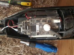 Wnętrze urządzenia z płytką elektroniki, przewodami i złączem; obok widać śrubokręty na dywanie