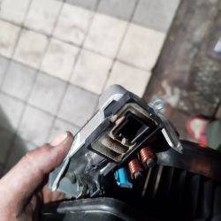 Widok zbliżeniowy na element elektroniczny z dwoma cewkami miedzianymi, trzymany w brudnej dłoni.
