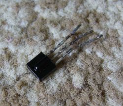 Close-up view of a black three-pin component lying on a carpet-like surface.