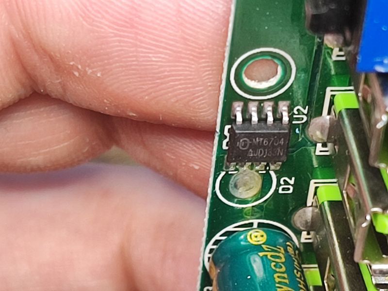 Zbliżenie na płytkę drukowaną z widocznym układem scalonym MT6704 oraz fragmentami portów USB i kondensatora.