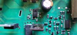 Zbliżenie płytki PCB z nadpalonym układem scalonym SMD obok kondensatora elektrolitycznego