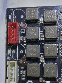 Zdjęcie płytki drukowanej (PCB) z czerwonym i białym złączem, uszkodzeniami wokół ścieżek oraz sześcioma cewkami indukcyjnymi oznaczonymi jako 220.