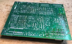 Spód płytki PCB ze starym tunerem satelitarnym na stole roboczym.