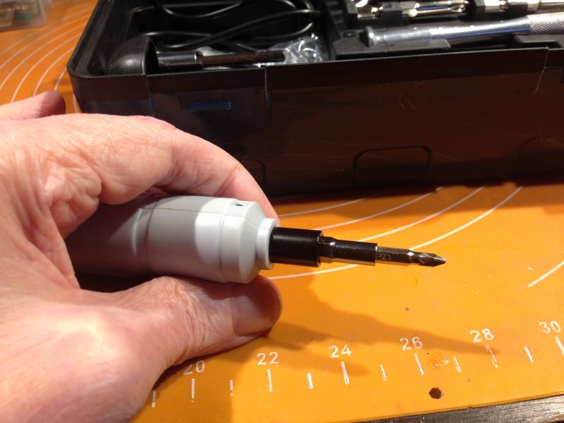 Ręka trzymająca elektryczny wkrętak z bitem na pomarańczowym tle.