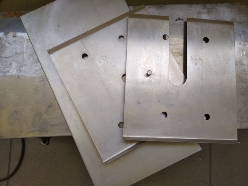 Trzy aluminiowe płytki ochronne z otworami, leżące na metalowej powierzchni.