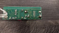 Spód zielonej płytki PCB z widocznymi ścieżkami i punktami lutowniczymi, leżącej na ciemnym blacie.