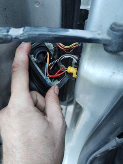A hand pointing at damaged electrical wires in a car.