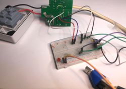 Breadboard with connected jumper wires and LED, next to an opened electrical socket with exposed PCB and wiring.