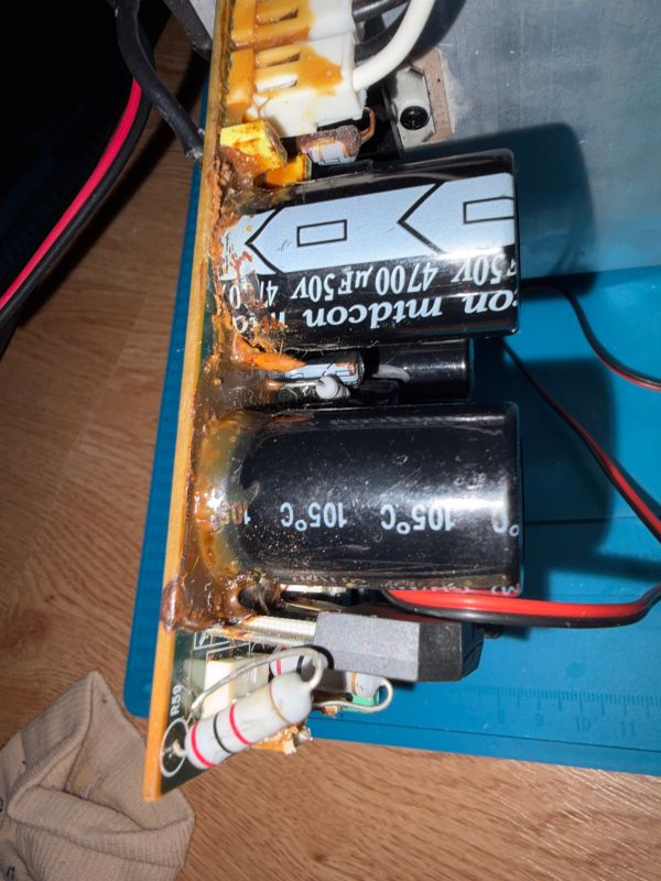 Uszkodzona płytka PCB z kondensatorami, zalana brązowym klejem i z wyraźnymi śladami nadpaleń