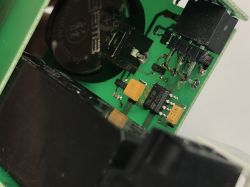 Zbliżenie na płytkę PCB z elementami elektronicznymi, baterią pastylkową i wyświetlaczem.