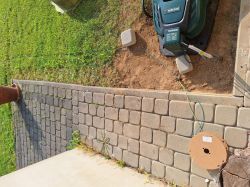 Robot koszący Parkside na stacji dokującej, kabel ograniczający ułożony na ziemi, cewka kabla położona na kostce brukowej.