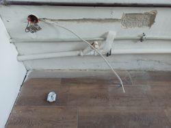 Widok na instalację elektryczną przy ścianie z przewodami i kontaktem leżącym na podłodze.