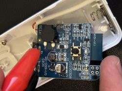 Close-up of a circuit board inside a white plastic case with a push button and a battery spring contact