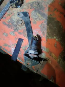 Niezainstalowany włącznik na pomarańczowej powierzchni obok kawałka metalu i nakrętki.