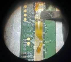 Zbliżenie na taśmę przyczepioną do płytki kontrolera z widocznym klejem i grotem lutownicy.