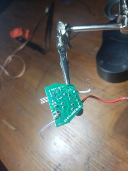 Circuit board with pin labels SDA, V+, and SCL, held in a tool holder.