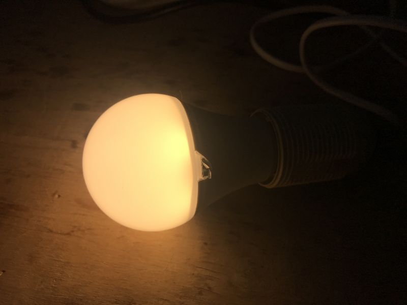Lit LED Bulb on Wooden Surface Lit LED bulb placed on a wooden surface.