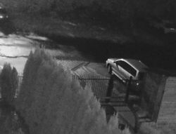 Nocne zdjęcie monitoringu przedstawiające samochód zaparkowany na podjeździe.