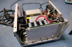 Wnętrze urządzenia elektronicznego z widocznymi komponentami, kablami i wentylatorem.