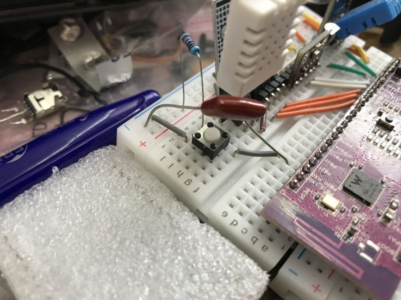 Close-up of a 100nF capacitor connected between a pin and ground on a breadboard.