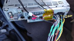 Zdjęcie tylnej części radia samochodowego z przymocowanymi kablami i modułem Bluetooth.