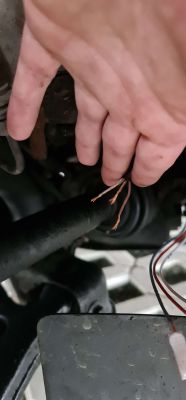 Ręka trzymająca trzy odsłonięte przewody pod maską samochodu.