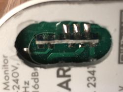 Close-up of a green circuit board visible through an opening in the metal casing of a device with partial technical specifications text.