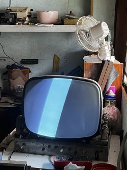 Stary kineskopowy telewizor z zniekształconym obrazem ustawiony na stole w warsztacie