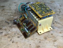 Two circuit boards with components and wires beside a white terminal module on a wooden workbench