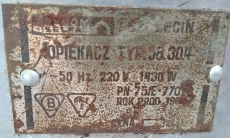 Rdzawe i zniszczone tabliczka znamionowa opiekacza typu JG 304 z czasów PRL, zawierająca podstawowe dane techniczne.